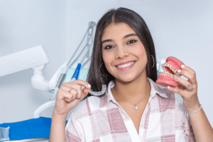 Smiling woman holding a clear aligner and a dental model with braces in an orthodontic office