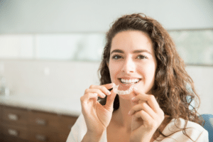 Smiling woman holding a clear orthodontic aligner near her teeth