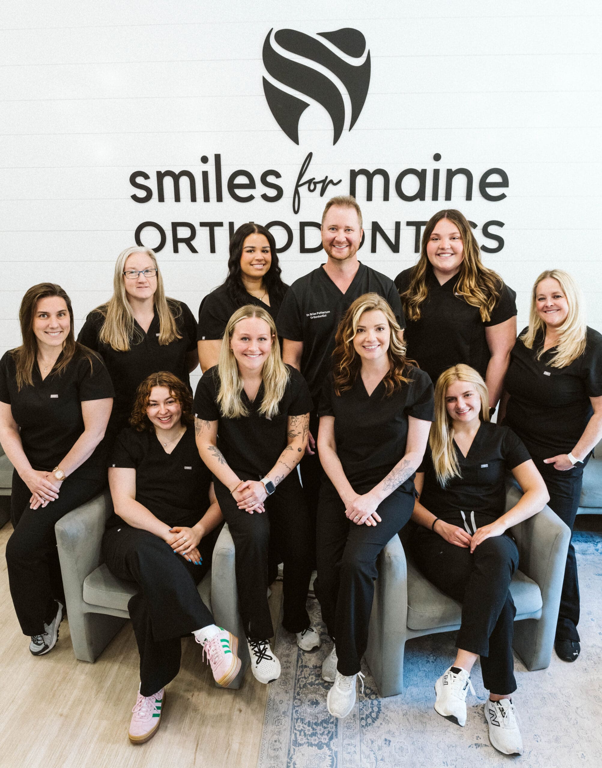 Smiles for Maine Orthodontics team posed together in front of the practice logo wall, reflecting their shared values of results and hospitality at Smiles for Maine Orthodontics in Waterville, ME