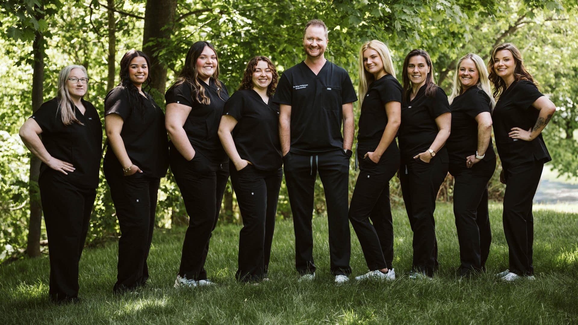 Orthodontic team standing together in a wooded outdoor setting, showcasing the friendly and approachable team at Smiles for Maine Orthodontics in Waterville, ME